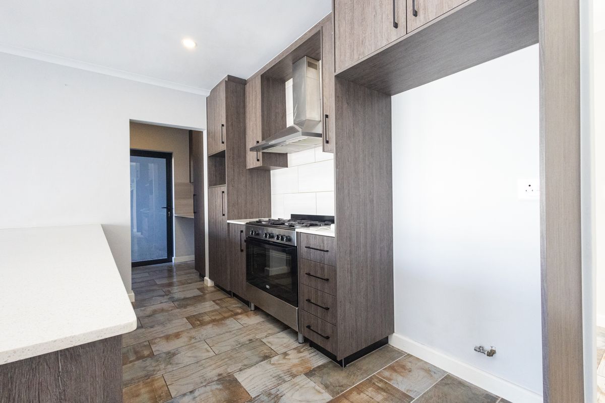 Modern kitchen featuring dark wood cabinetry, stone countertops, gas hob, oven, extractor fan, and tiled flooring, with an adjacent scullery area.