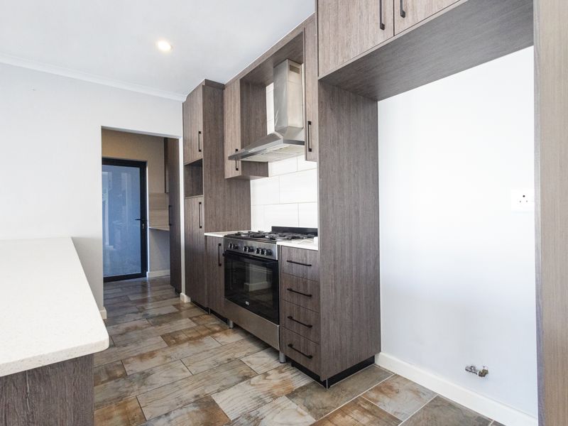 Modern kitchen featuring dark wood cabinetry, stone countertops, gas hob, oven, extractor fan, and tiled flooring, with an adjacent scullery area.
