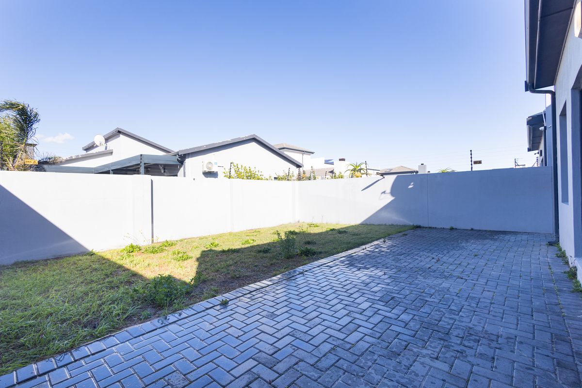 A private rear garden featuring a paved patio area and a lawn enclosed by high perimeter walls.