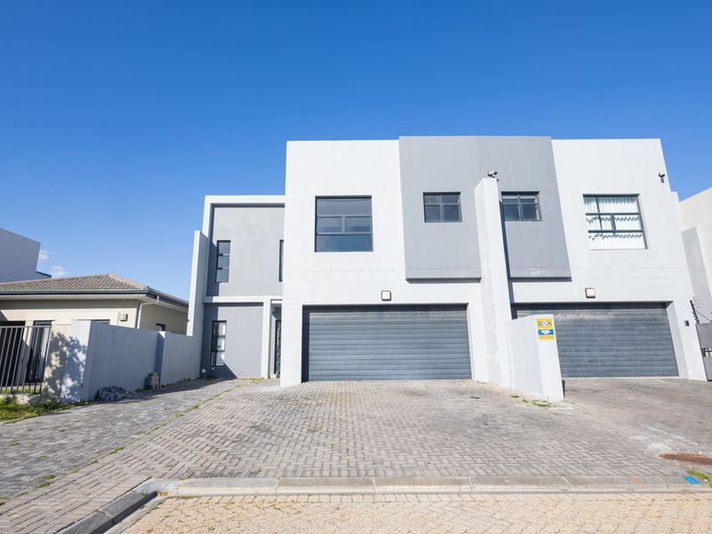 Modern double-story townhouse facade featuring a paved driveway, double garage, and secure perimeter fencing.