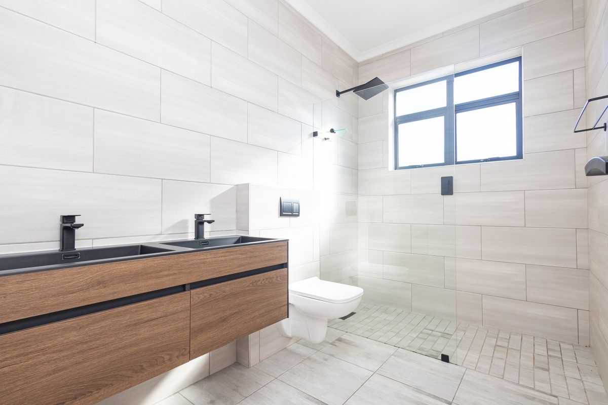 Modern bathroom featuring a double vanity with matte black fixtures, a wall-mounted toilet, and a spacious walk-in shower with a rain shower head.