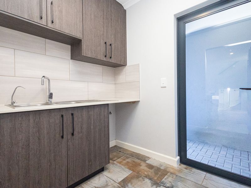 A modern, well-maintained laundry area featuring built-in cabinetry, stone countertops, a stainless steel sink, and direct access to an outdoor paved area.