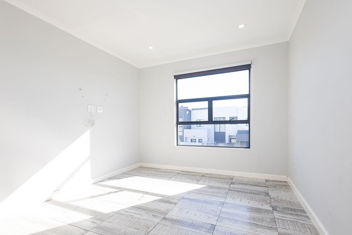 A bright, empty bedroom featuring modern tiled flooring, recessed downlights, and a large window with a roller blind.