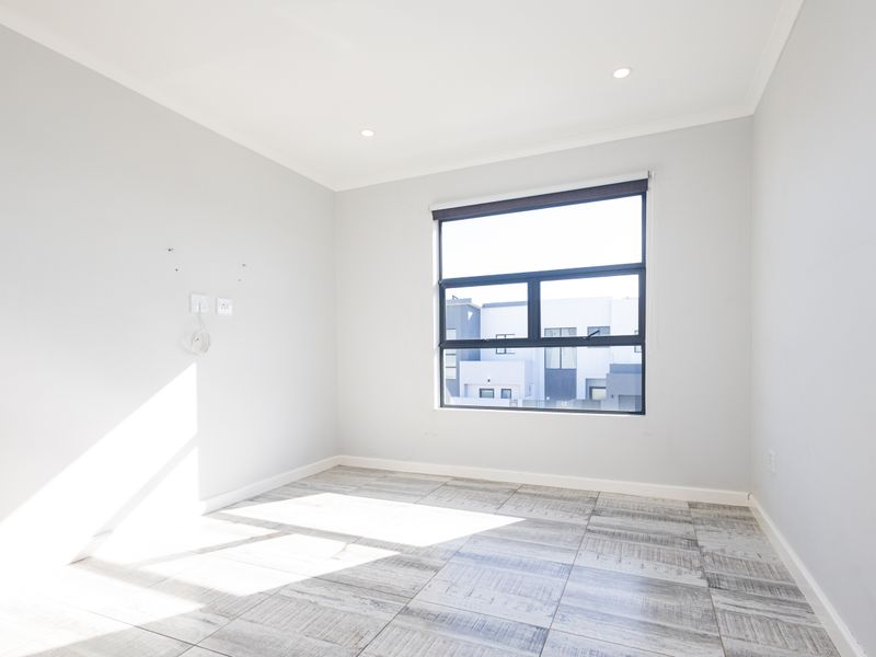 A bright, empty bedroom featuring modern tiled flooring, recessed downlights, and a large window with a roller blind.