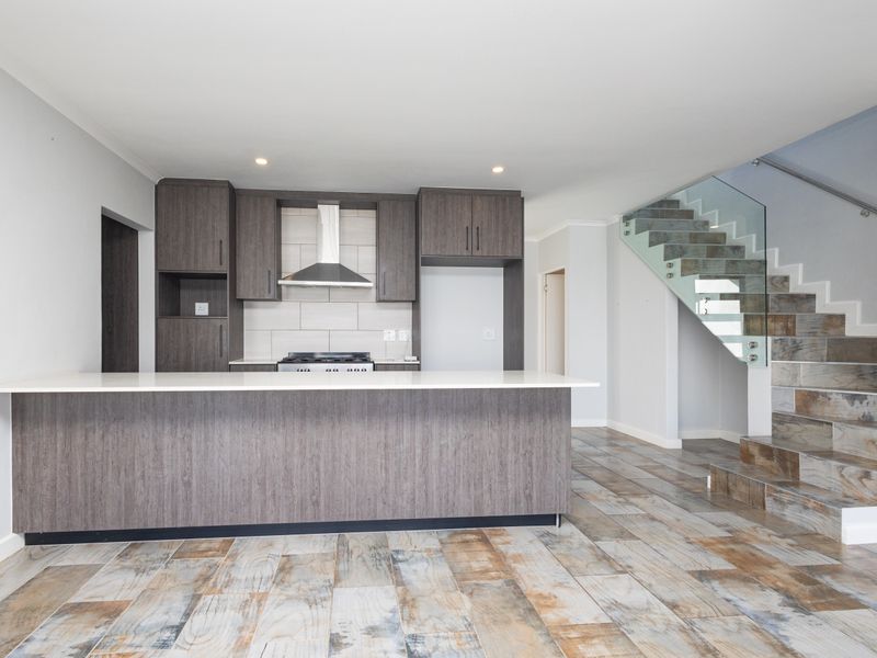 Modern open-plan kitchen featuring dark wood cabinetry, a central island, and a striking staircase with glass balustrades and decorative tiled steps.
