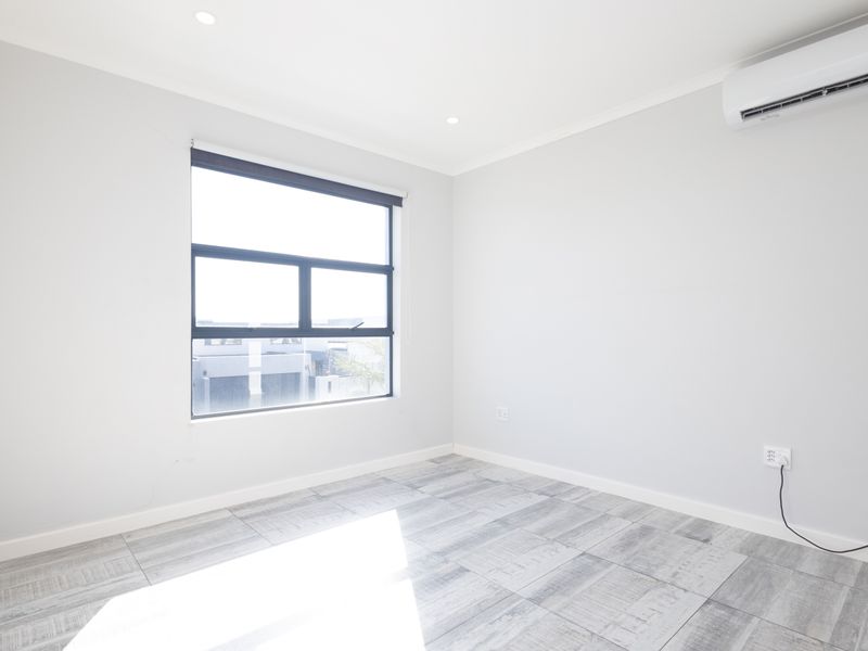 A bright, empty bedroom featuring modern grey tiled flooring, recessed downlighting, and a wall-mounted split-system air conditioning unit.