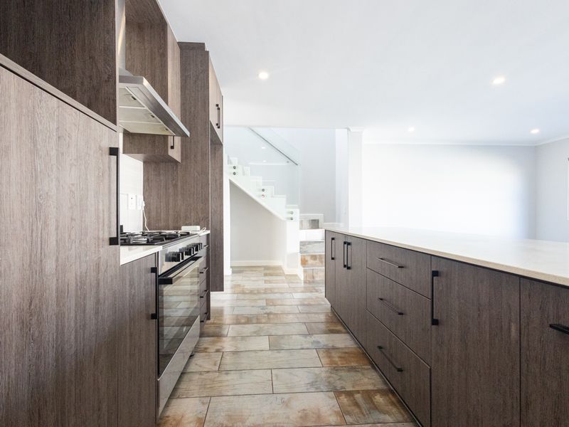 Modern kitchen featuring dark wood cabinetry, stone countertops, integrated appliances, and tiled flooring, leading to an open-plan living area with a staircase.