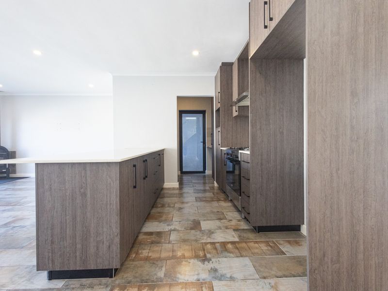 Modern kitchen featuring dark wood-grain cabinetry, stone benchtops, and tiled flooring, flowing into an open-plan living area with a built-in fireplace.