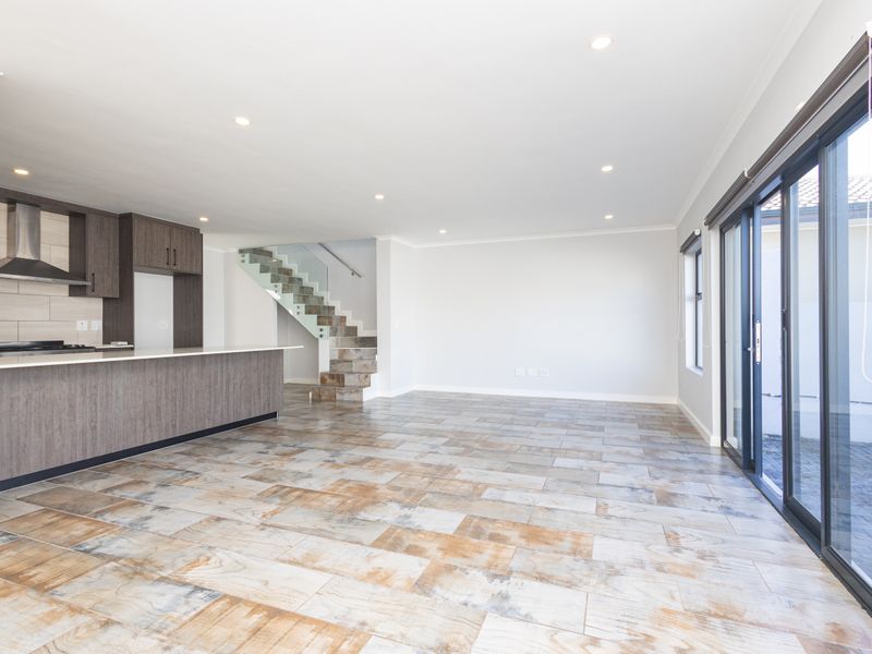 Spacious open-plan living area featuring a modern kitchen with built-in cabinetry, a contemporary staircase with glass balustrade, and large sliding doors leading outdoors.