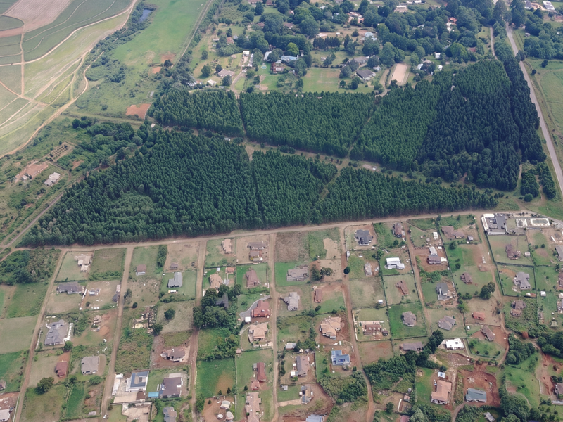 An aerial view of a residential area featuring multiple plots of land adjacent to a large forested area and surrounding agricultural fields.