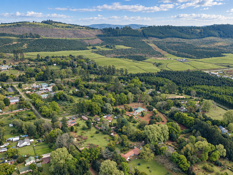 An expansive aerial view of a rural residential area surrounded by lush green hills, forests, and open landscape.