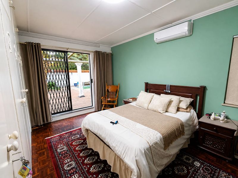 A well-maintained bedroom featuring parquet flooring, built-in cupboards, and a split-system air conditioner, with direct access to an outdoor patio area.