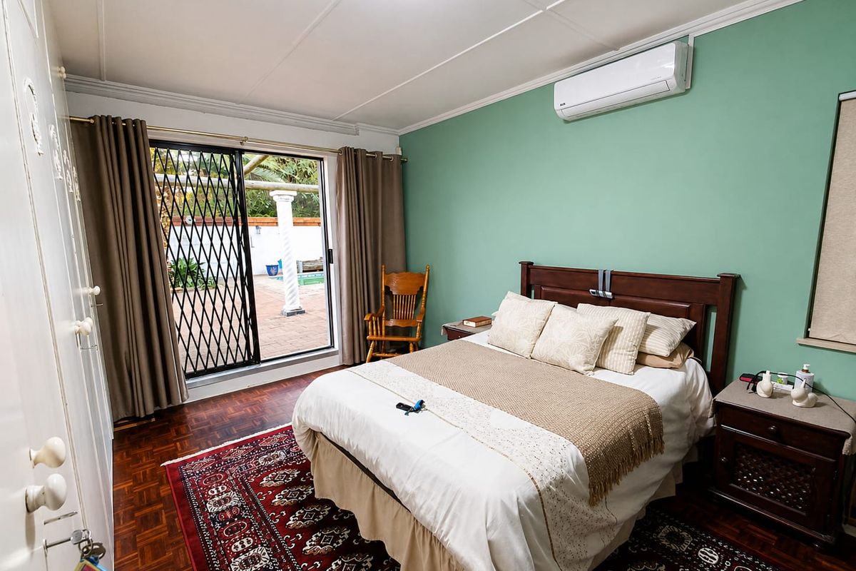 A well-maintained bedroom featuring parquet flooring, built-in cupboards, and a split-system air conditioner, with direct access to an outdoor patio area.
