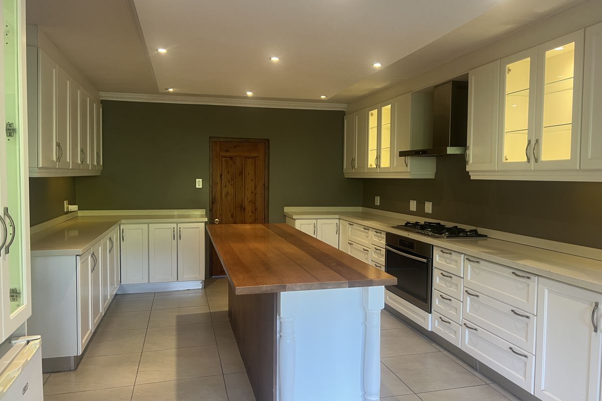 Spacious kitchen featuring white cabinetry, a central wooden island, built-in oven and gas hob, recessed lighting, and neutral tiled flooring.