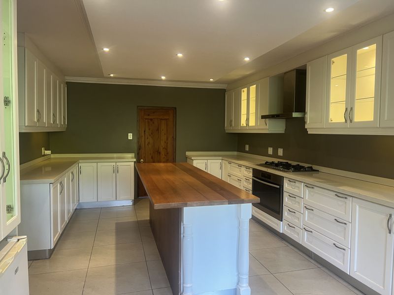 Spacious kitchen featuring white cabinetry, a central wooden island, built-in oven and gas hob, recessed lighting, and neutral tiled flooring.