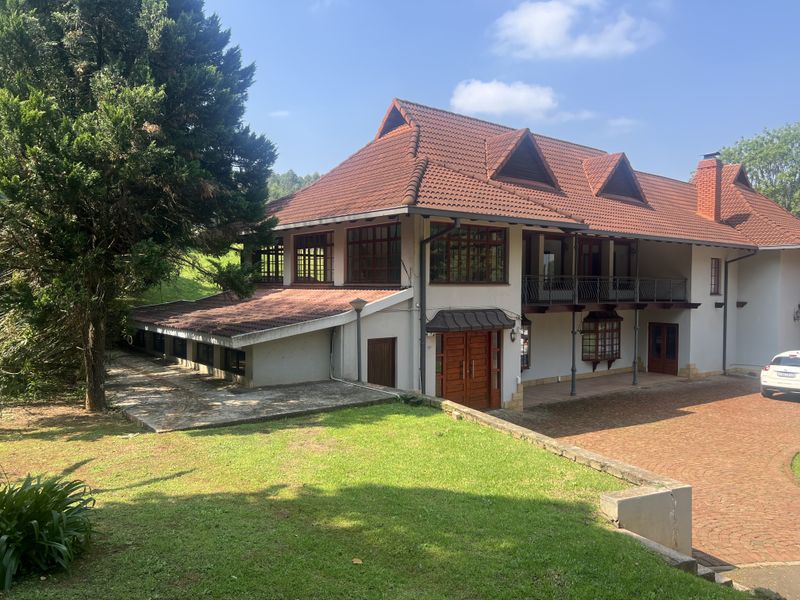 A large multi-story residence featuring a classic tiled roof, timber window frames, a spacious brick driveway, and a covered balcony area.