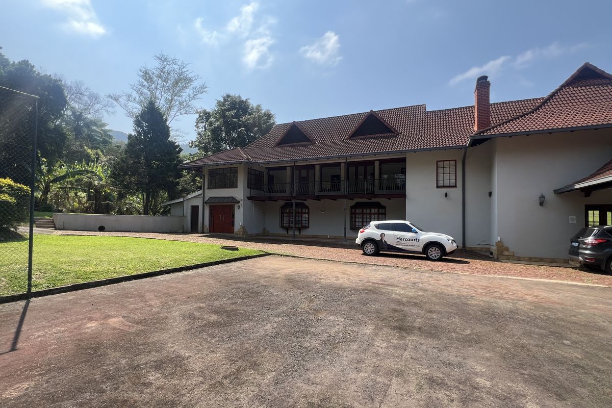 Rear view of a large two-story residence featuring a terracotta tile roof, upper-level balcony, and extensive brick-paved driveway area.