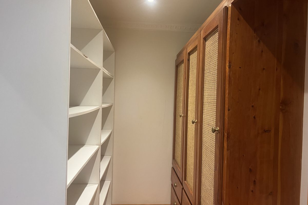 A walk-in wardrobe or dressing area featuring built-in white shelving and a wooden wardrobe unit with cane paneling.
