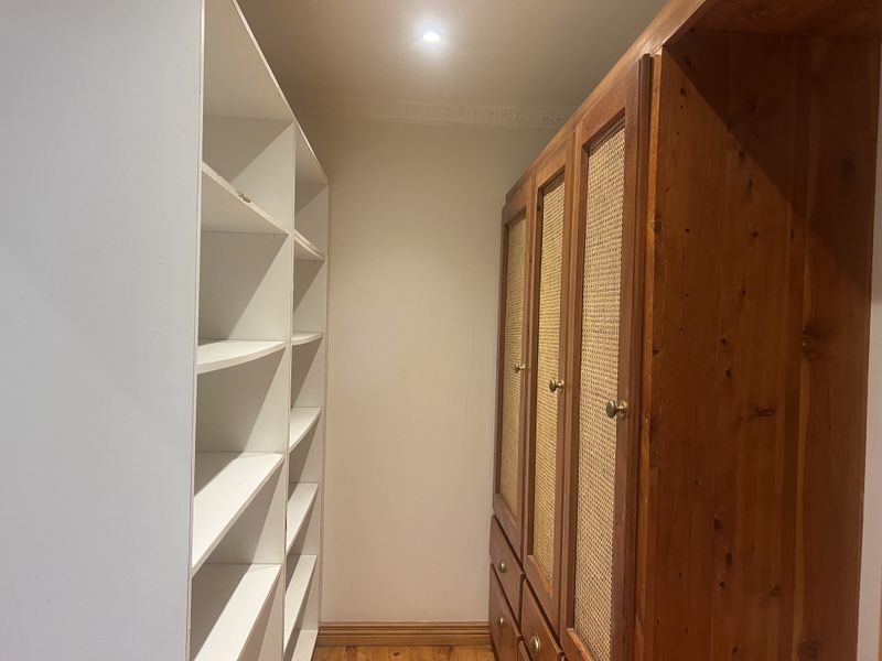 A walk-in wardrobe or dressing area featuring built-in white shelving and a wooden wardrobe unit with cane paneling.