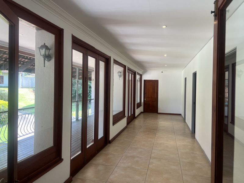 A bright, spacious hallway featuring tiled flooring, recessed lighting, and multiple timber-framed glass doors providing access to the outdoor patio area.
