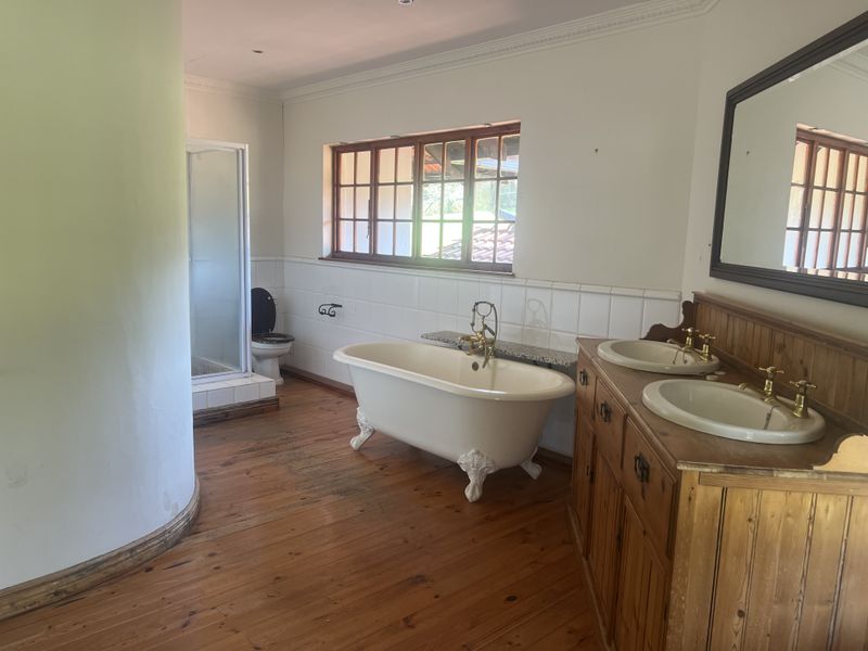Spacious bathroom featuring a classic clawfoot bathtub, double vanity with wooden cabinetry, separate shower enclosure, and timber flooring.