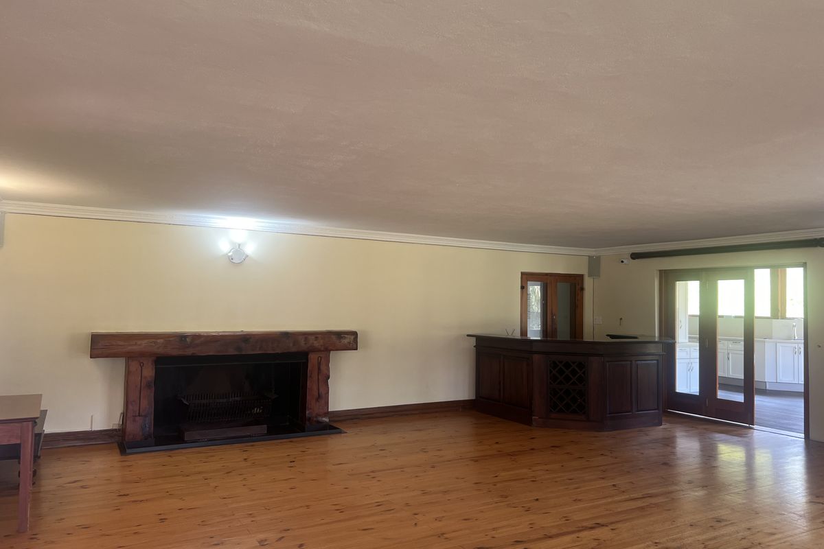 Spacious living area featuring polished timber flooring, a prominent built-in fireplace with a timber mantel, and a custom built-in bar.