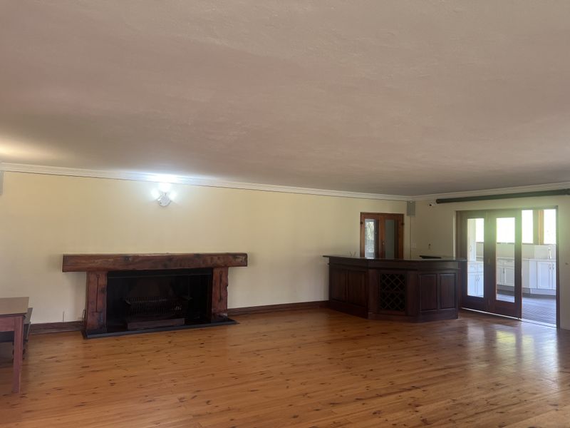 Spacious living area featuring polished timber flooring, a prominent built-in fireplace with a timber mantel, and a custom built-in bar.