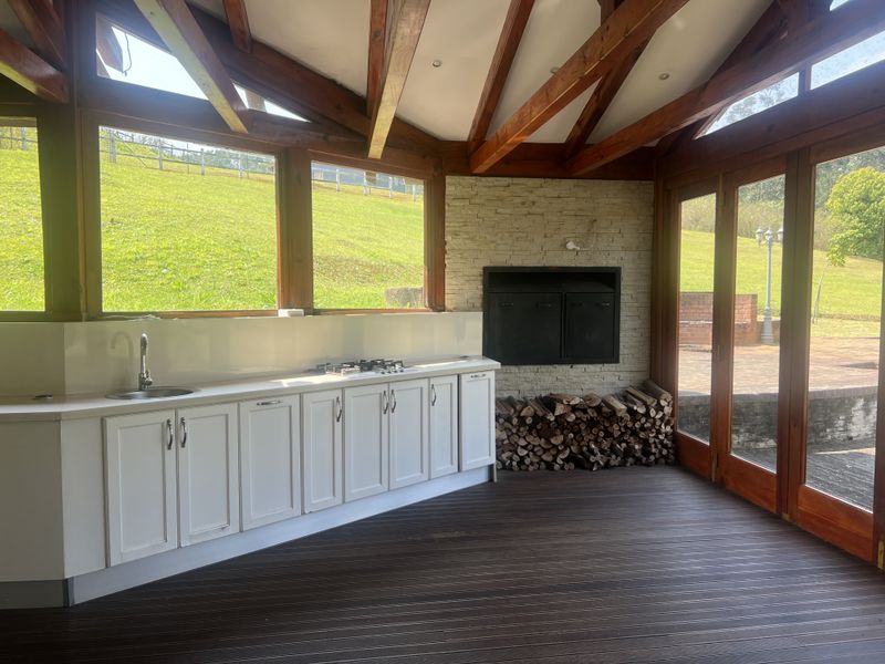 Covered patio featuring timber decking, exposed beams, built-in braai with stone cladding, and a functional kitchenette with sink and gas hob.