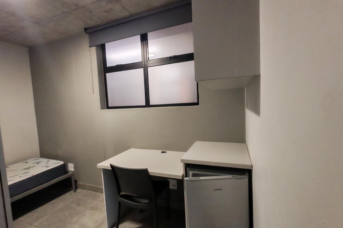 A compact bedroom featuring an exposed concrete ceiling, tiled flooring, and a built-in desk area with integrated cabinetry.