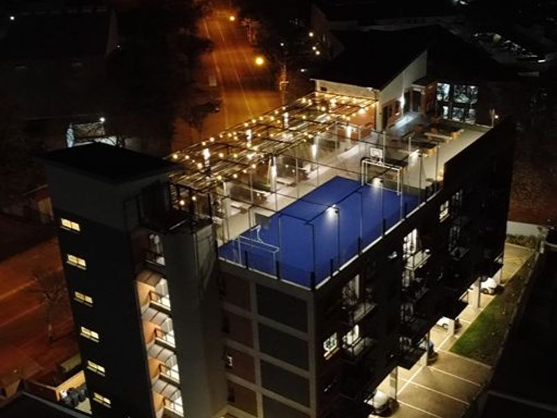 Aerial night view of an apartment building featuring a rooftop sports court, integrated lighting, and ground-level parking facilities.