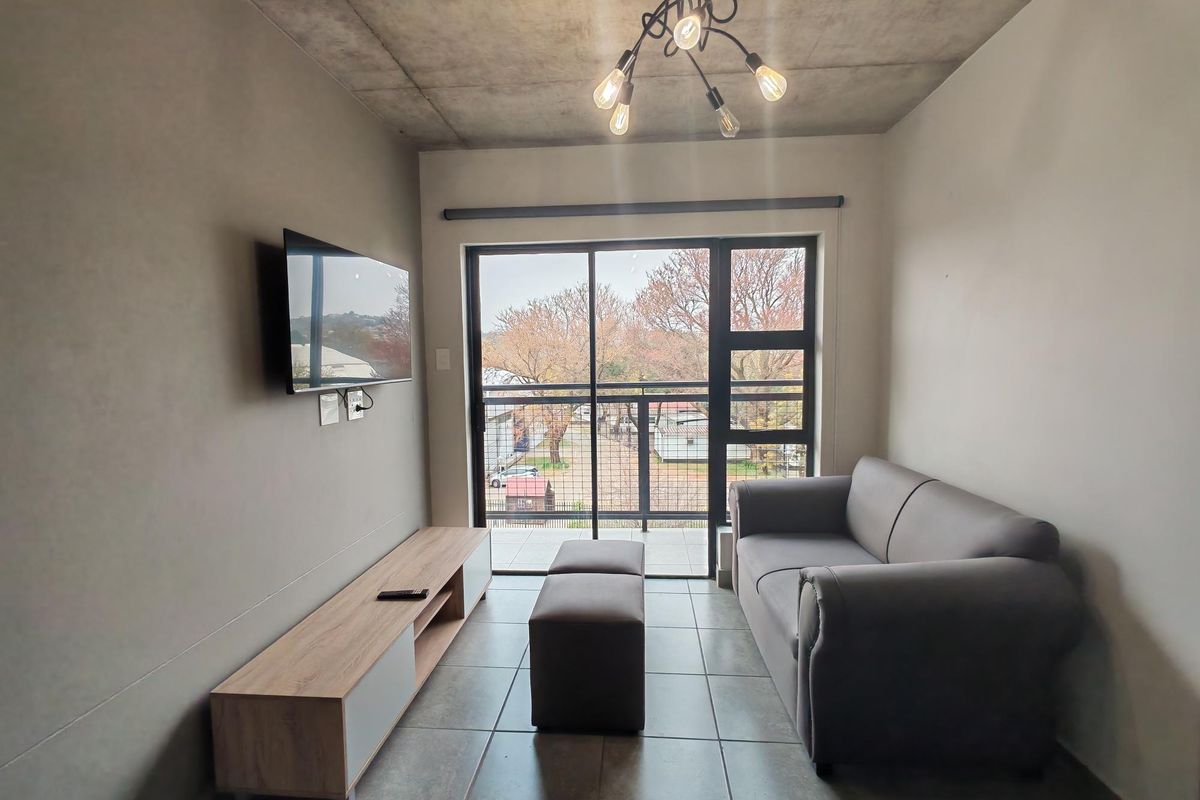 Modern living room featuring an exposed concrete ceiling, tiled floors, and a sliding glass door leading to a balcony with neighborhood views.