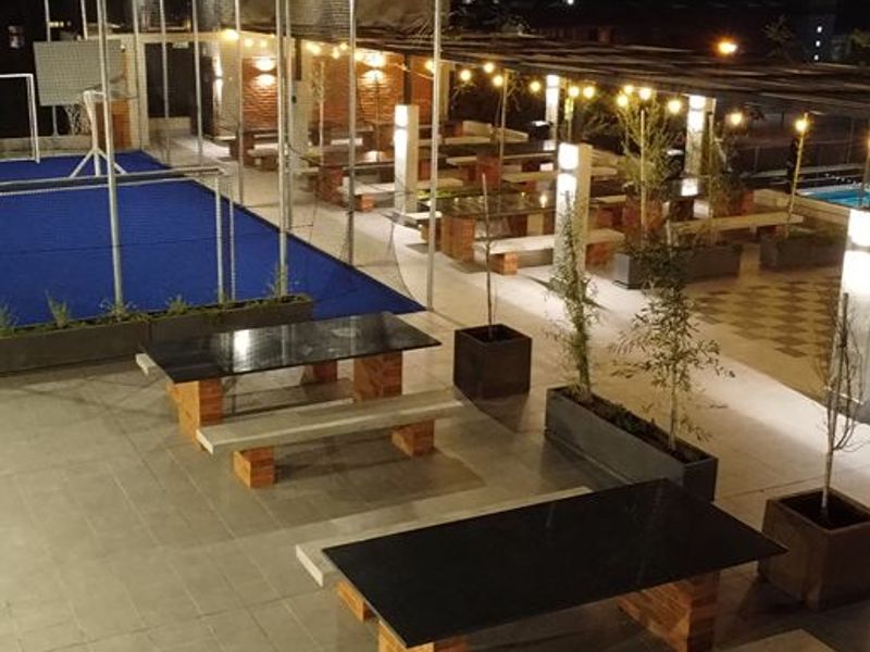 A well-maintained outdoor sports and entertainment area featuring a padel court, integrated brick seating, and ambient string lighting.