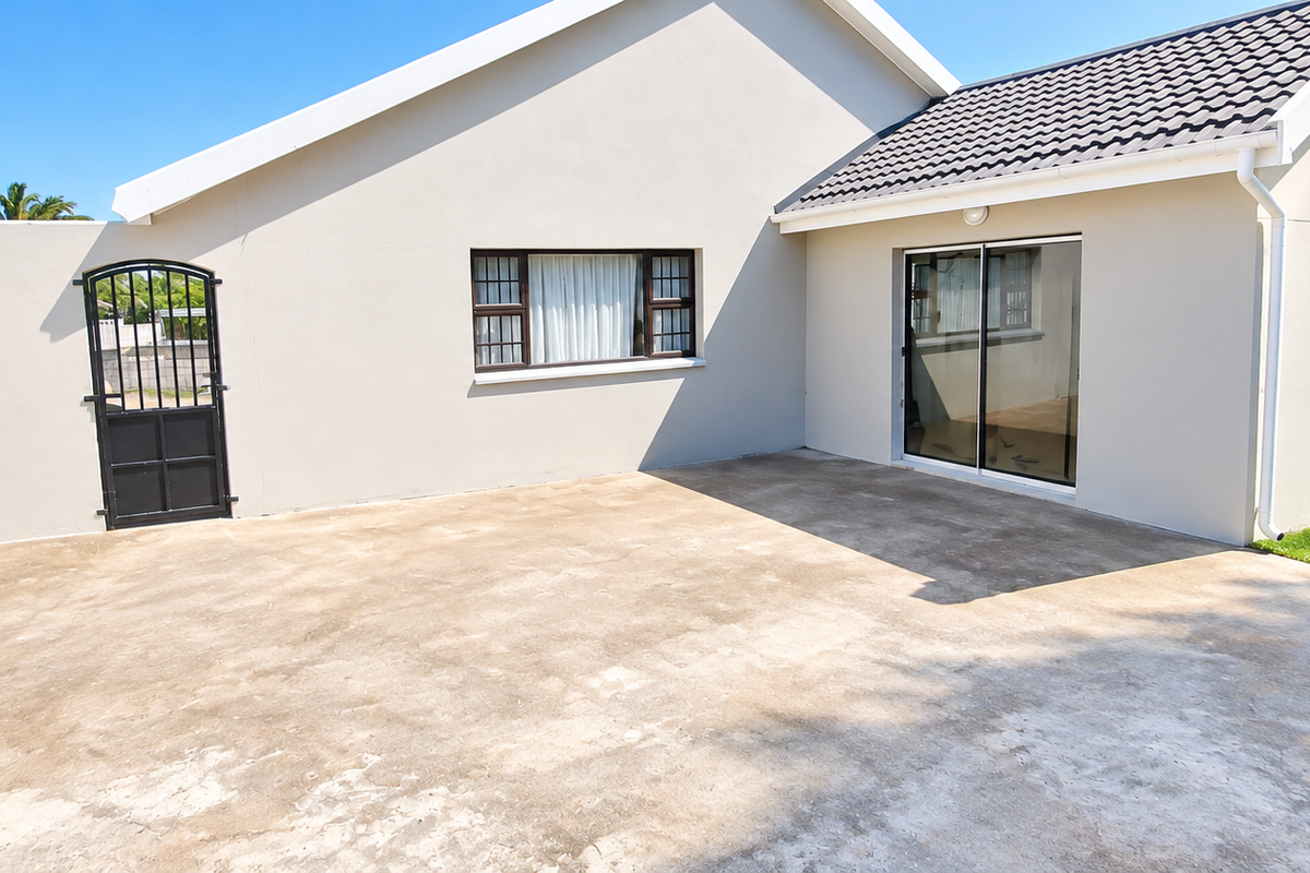 Rear exterior view featuring a spacious concrete patio, built-in brick braai, and direct access to the home via sliding glass doors.