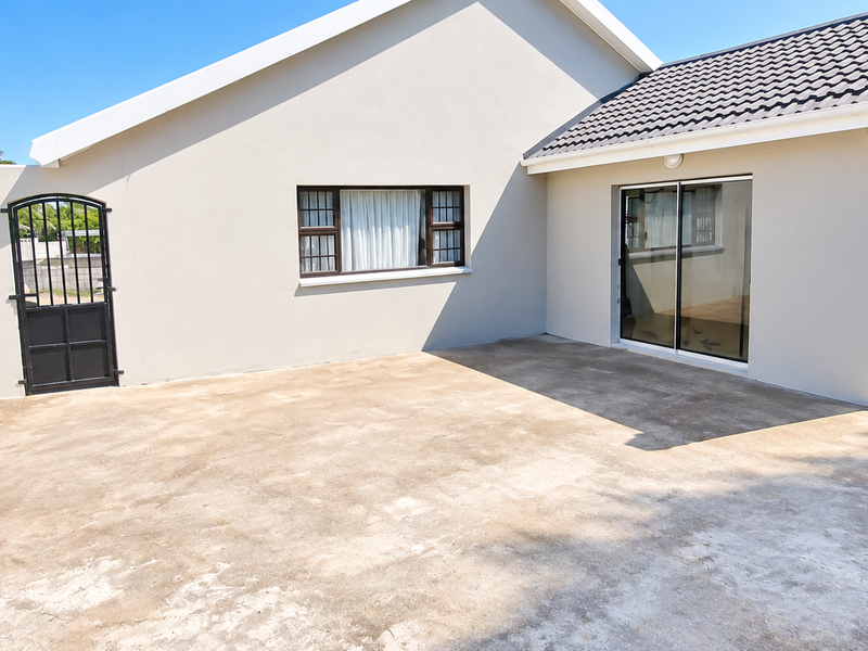 Rear exterior view featuring a spacious concrete patio, built-in brick braai, and direct access to the home via sliding glass doors.