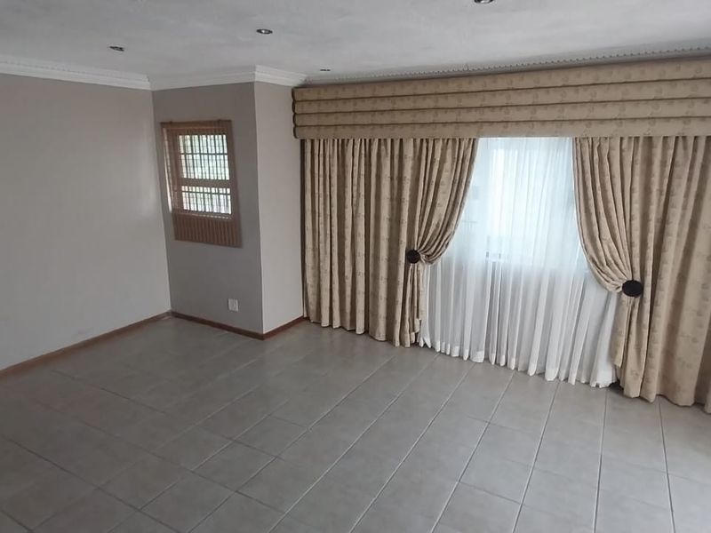 A spacious, empty living room featuring neutral wall tones, tiled flooring, recessed lighting, and decorative cornicing, ready for personalization.