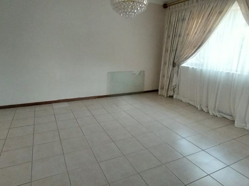 An empty living room featuring tiled flooring and a crystal chandelier, requiring minor wall repairs to restore the space.