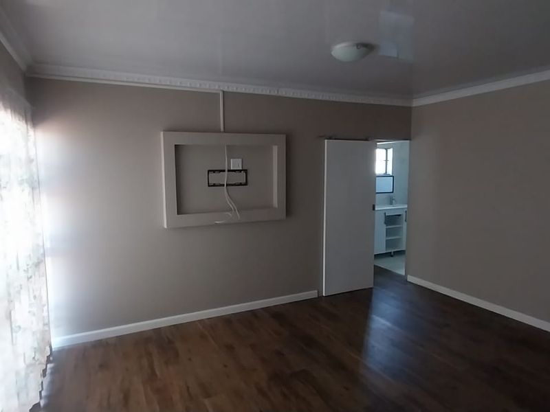 Spacious living room featuring laminate flooring, a built-in media niche, and decorative ceiling cornicing, offering a clean and neutral canvas.