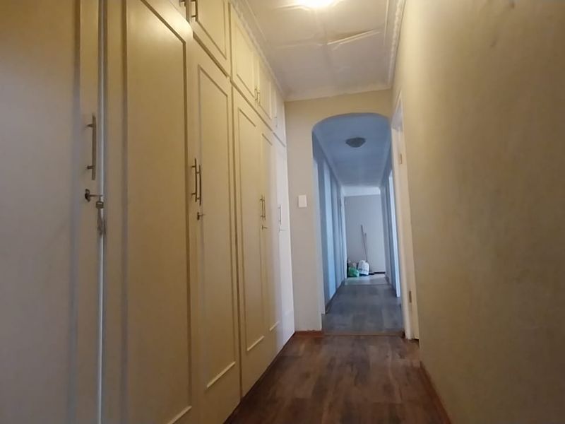 A narrow hallway featuring extensive built-in storage cupboards, laminate flooring, and an arched transition leading to an adjacent corridor.