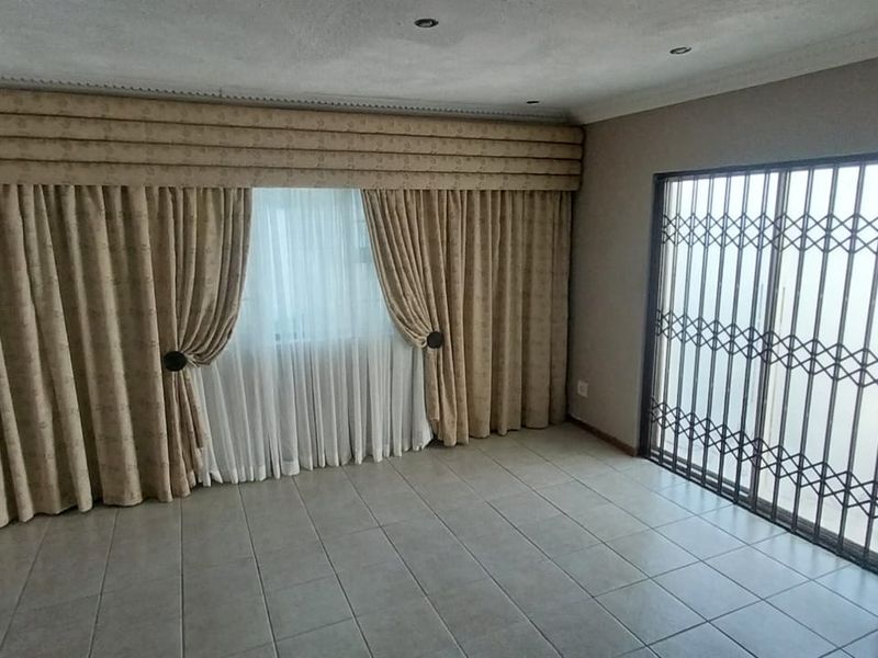 An empty living room featuring neutral tiled flooring, recessed downlighting, decorative cornicing, and a sliding security gate leading to the exterior.