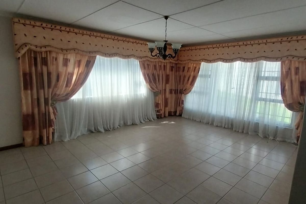Spacious living area featuring neutral tiled flooring, a drop ceiling, and large windows with extensive drapery.