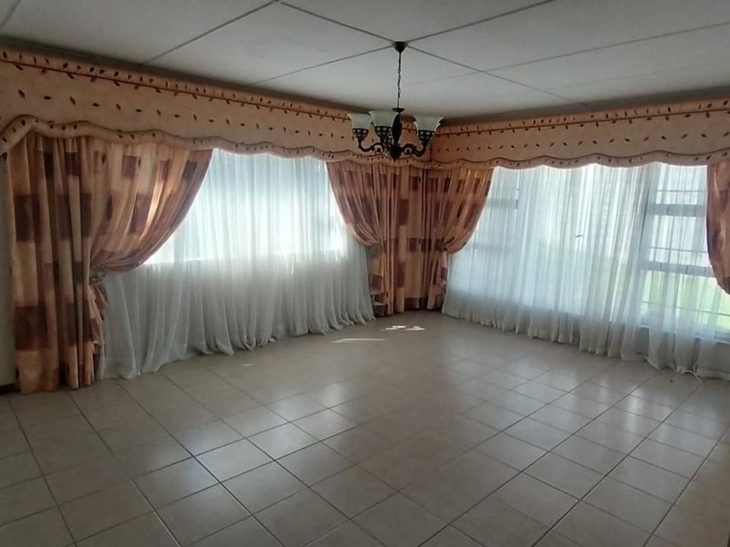 Spacious living area featuring neutral tiled flooring, a drop ceiling, and large windows with extensive drapery.