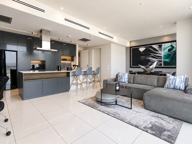 Modern open-plan living area featuring a sleek kitchen with dark cabinetry, a central island, and high-end finishes throughout the spacious, well-lit interior.