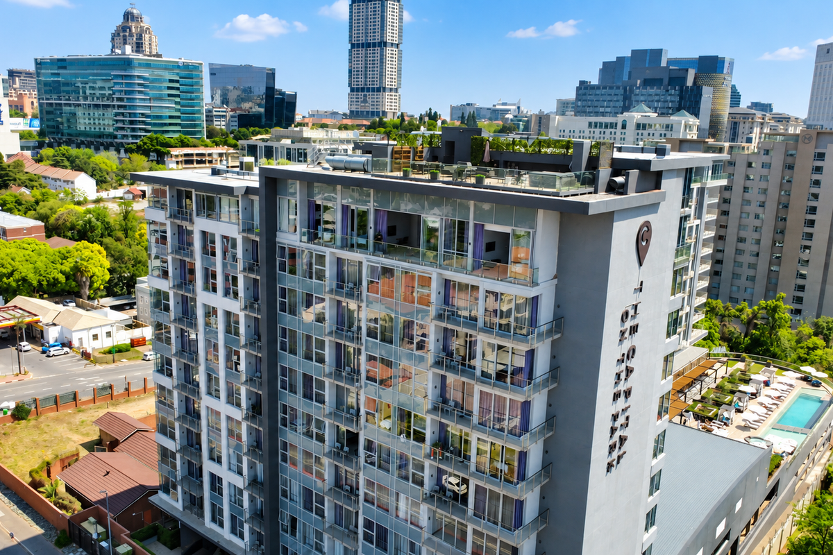 Aerial view of a modern high-rise penthouse building featuring glass balconies, a rooftop terrace, and an outdoor swimming pool in an urban setting.