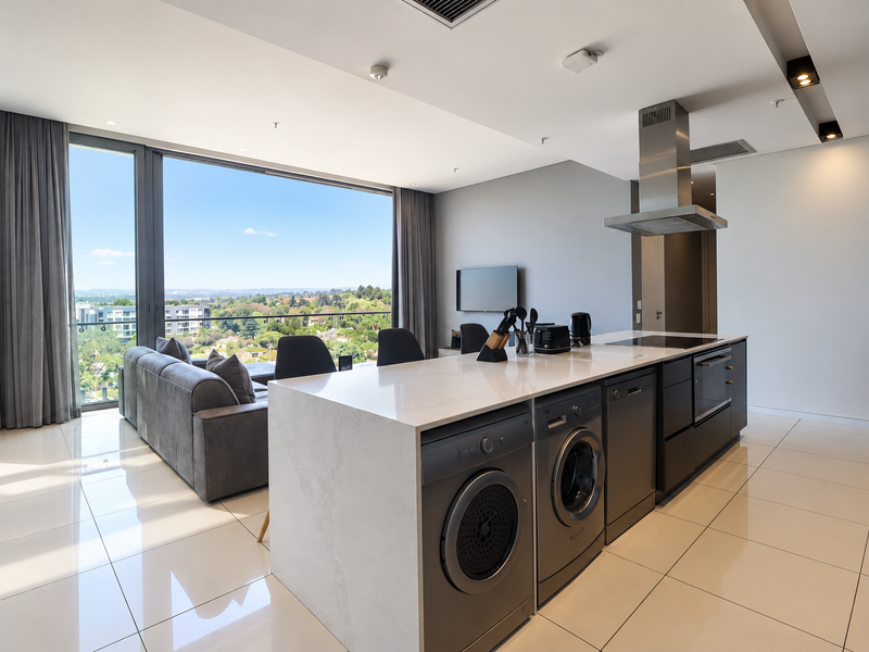 Modern open-plan living area featuring a sleek kitchen island with integrated appliances, high-gloss floor tiles, and expansive windows offering panoramic views.