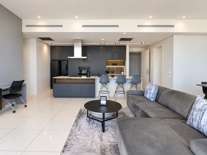 Modern open-plan living area featuring a sleek kitchen with a central island, integrated appliances, and ducted air conditioning throughout the space.