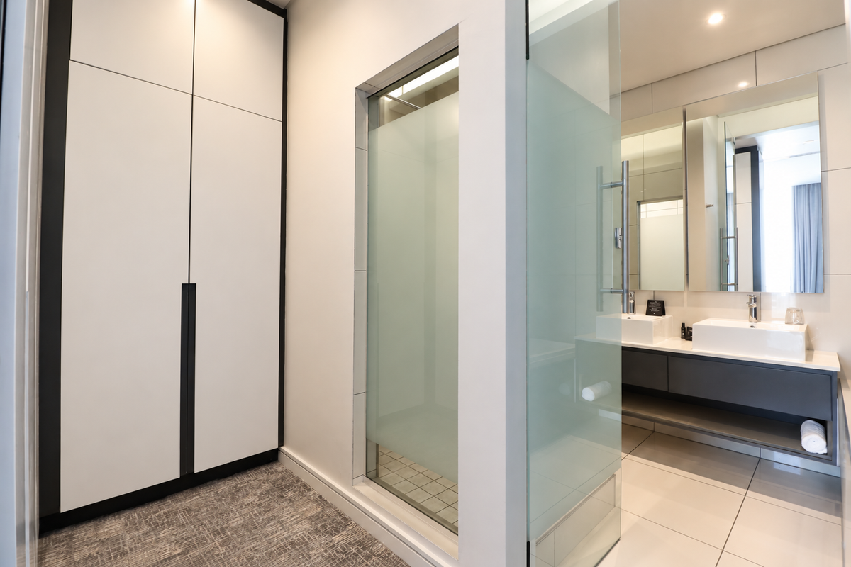 Modern bathroom featuring a double vanity, sleek cabinetry, and a private frosted glass shower enclosure with high-quality finishes.