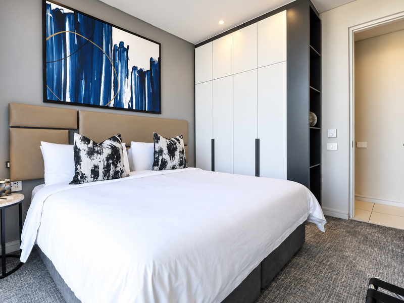 Modern bedroom featuring a built-in wardrobe, integrated headboard, and neutral carpeted flooring, offering a clean and contemporary living space.