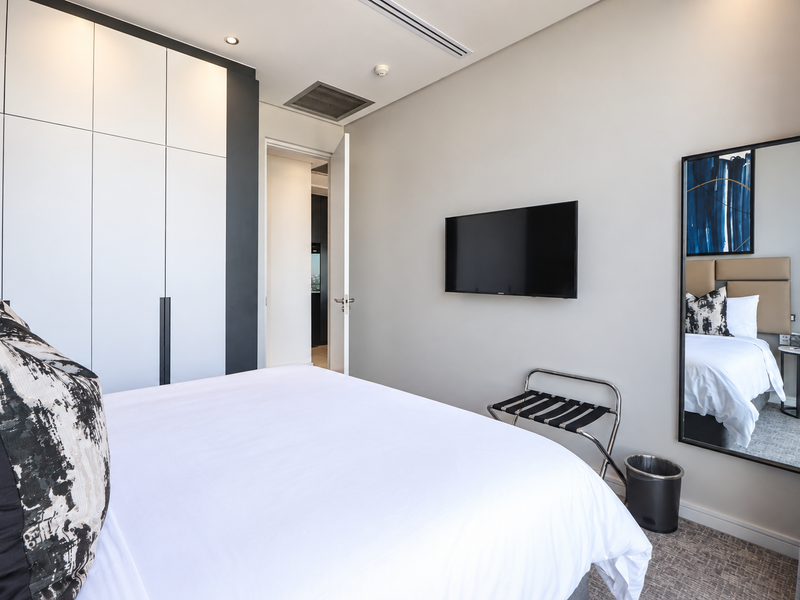 Modern bedroom featuring built-in floor-to-ceiling cupboards, recessed lighting, ducted air conditioning, and a wall-mounted television.