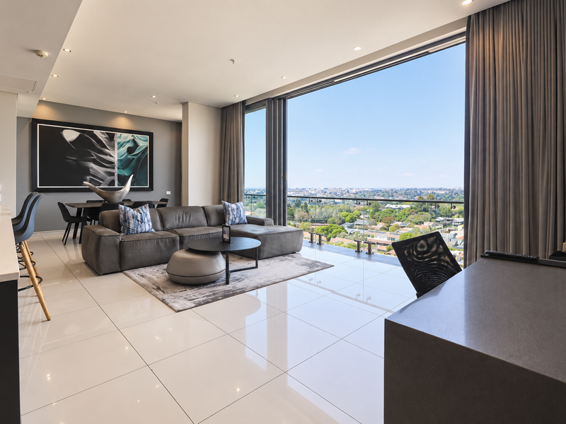 Modern open-plan living area featuring sleek porcelain tiles, recessed lighting, and expansive floor-to-ceiling glass doors opening to a balcony with panoramic city views.