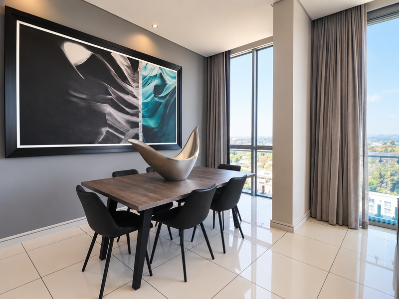 Modern dining area featuring large floor-to-ceiling windows with expansive views, sleek porcelain tile flooring, and recessed lighting in a contemporary penthouse setting.